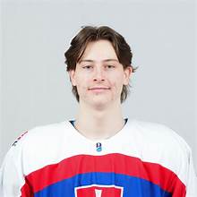 Portrait of a young male hockey player wearing a red, white, and blue jersey with a neutral expression, set against a gray background.