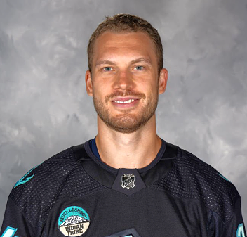 Portrait of a smiling male hockey player wearing a black team jersey with logos.